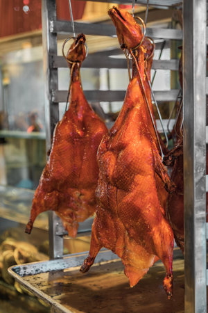 Traditional Chinese whole roasted Peking duck hanging on roasting hooks in the kitchen at a Chinese restaurant in San Franciscoの写真素材