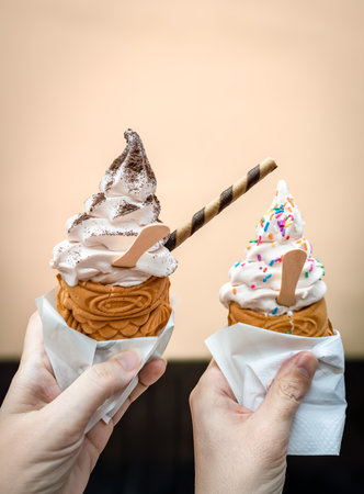 Two hands hold taiyaki Japanese ice cream cones with soft serve and chocolate and sugar sprinkles toppingsの写真素材