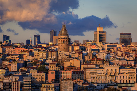 Cityscape above the Golden Horn, bathed in golden hour sunset light under dramatic clouds, the Galata Tower rising prominently in Istanbul, Turkeyの写真素材
