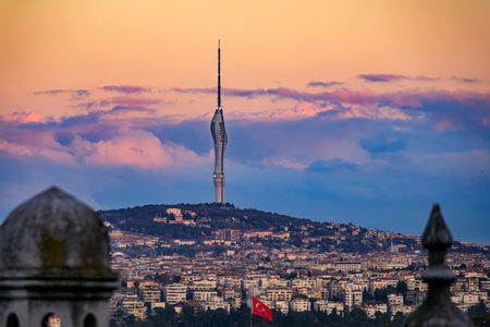 An iconic view of the Camlica TV Tower rising above the Istanbul cityscape and a foreground mosque dome at sunset golden hour, in Istanbul, Turkeyの写真素材