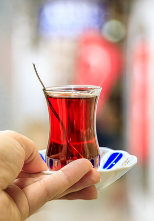 Woman s hand holds a traditional tulip shaped glass of Turkish black tea or chai with an ornate...