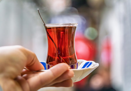 Woman s hand holds a traditional tulip shaped glass of Turkish black tea or chai with an ornate...