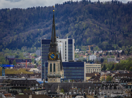 An aerial view of the city skyline with its historic buildings, prominent church spires, and forested hills under a cloudy sky in Zurich, Switzerlandの写真素材