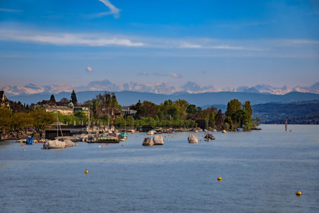 A beautiful serene view of boats on Lake Zurich with the snow covered majestic Swiss Alps visible in the background in Zurich, Switzerlandの写真素材