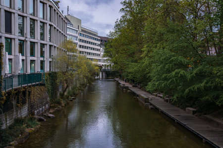 A quiet urban canal, the Schanzengraben, lined with a wooden boardwalk and lush green trees along...