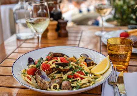 Pasta linguini with fresh clams and cherry tomatoes with a glass of white wine at an Italian restaurant in of Nice, South of Franceの写真素材