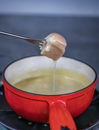Traditional Swiss fondue of melted cheese dripping from a piece of bread into a red pot, a quintessential dining experience in Zurich, Switzerlandの写真素材