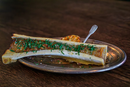 A gourmet dish of roasted bone marrow topped with a fresh herb garnish, served with a grilled lemon on a platter at a restaurant, Zurich, Switzerlandの写真素材