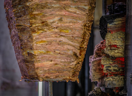 A rotating spit with seasoned, thinly sliced lamb slowly cooking at a traditional kebab shop, ready...