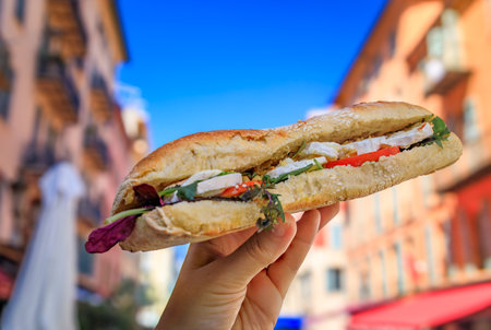 Woman s hand holds a freshly made mozzarella, tomato and arugula French baguette sandwich in the old town or Vieille Ville, Nice, Franceの写真素材
