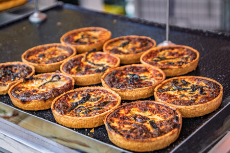 Selection of freshly baked quiches with vegetables, golden brown tops, on display at an artisanal...