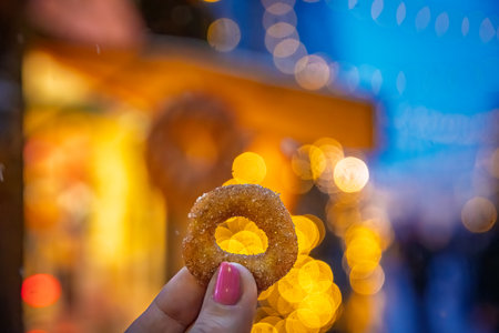 Woman holds a golden brown mini donut, sprinkled with sugar and cinnamon, a traditional snack at the Zurich Christmas Market, Switzerlandの写真素材