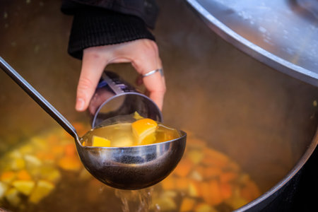 Vendor pours white mulled wine with oranges from a boiling pot into a cup, steam coming up, festive scene at the Strasbourg Christmas Market in Franceの写真素材