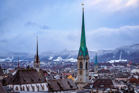Aerial winter cityscape with iconic church towers, terracotta tile roofs, and snow covered Uetliberg mountain after a snowfall in Zurich, Switzerlandの写真素材