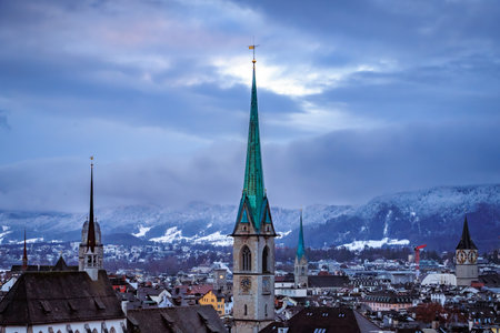 Aerial winter cityscape with iconic church towers, terracotta tile roofs, and snow covered Uetliberg mountain after a snowfall in Zurich, Switzerlandの写真素材