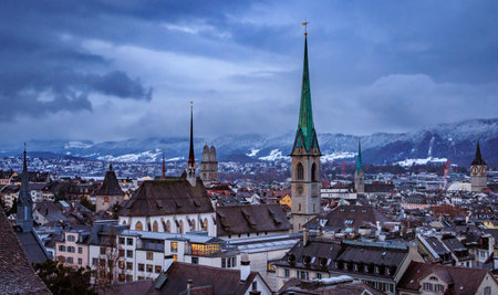 Aerial winter cityscape with iconic church towers, terracotta tile roofs, and snow covered Uetliberg mountain after a snowfall in Zurich, Switzerlandの写真素材