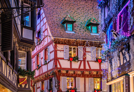 Festive decorations and ornaments on historic half timbered houses glow at sunset during the Christmas Market in the Old Town, Colmar, Alsace, Franceの写真素材