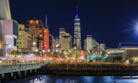 The illuminated cityscape and skyline of Lower Manhattan with modern skyscrapers at night from a waterfront park in New York City, USAの写真素材