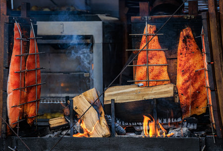 Salmon fillet roasting on wooden planks over open fire, glowing embers and smoke create a rustic...