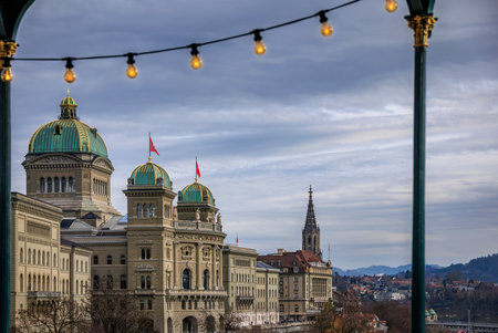A string of warm Christmas lights of the Christmas Market frame a winter view of the Federal Palace and Minster spire at twilight in Bern, Switzerlandの写真素材