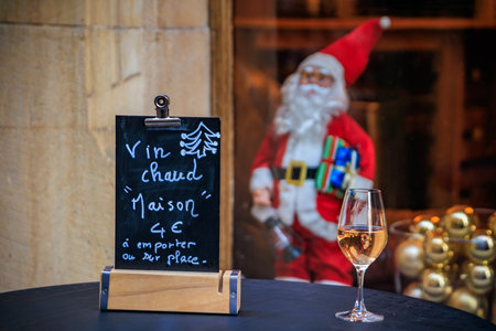 Glass of Gewrtzraminer white wine on an outdoor table next to a handwritten sign, blurred Santa Claus in the background in Colmar, France at Christmasの写真素材
