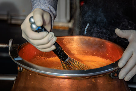 Steaming caramel whisked in a large copper pot for coating almonds at a festive Christmas market in Bern, Switzerland, creating a cozy holiday sceneの写真素材
