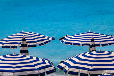 Striped umbrellas on a beach along Promenade des Anglais with the turquoise water of the Mediterranean Sea in the background in Nice, South of Franceの写真素材