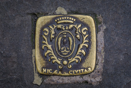 Antique metal manhole cover with the coat of arms of the city of Nice with an eagle and crown on the street pavement in the Old Town, Nice, Franceの写真素材