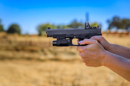 Woman s hand holding a modern semi automatic .40 caliber pistol with a red dot laser sight at an...