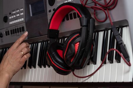 Stylish black-red headphones and a female hand on a background of synthesizer keys.