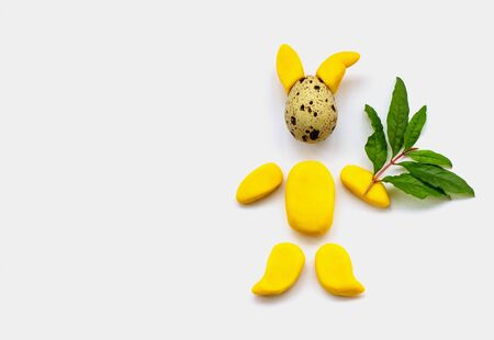 Children's craft of an Easter bunny from a quail egg and yellow plasticine on a white background. Easter bunny made from eggs and plasticine with a green twig. Copy space, childhood, easter.の写真素材