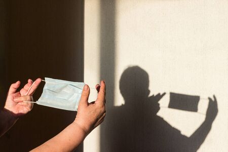 Shadow of a hand puts on a protective medical mask, copy space. Protection against coronavirus infection covid-19. Silhouette of hands with a medical mask for protection against coronavirusの写真素材