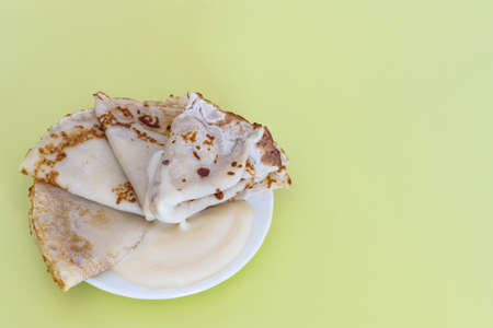 Russian national dish, pancakes with condensed milk on a white plate on a yellow background. Copy...