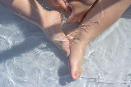 Baby feet bathing in a blue plastic pool. A little kid bathes in a transparent pool with dandelions....