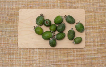 Green feijoa fruits on a wooden board on a brown tablecloth. Feijoa tropical fruit. Top view, frame....