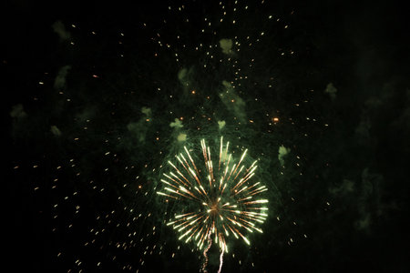Bright fireworks with a green glowing center with green sparks and smoke, against the background of the night sky. Beautiful colorful festive fireworks against the black sky, long exposure.の写真素材