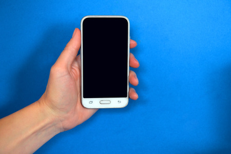 Phone in the left hand on a blue background. Gadget in hand.