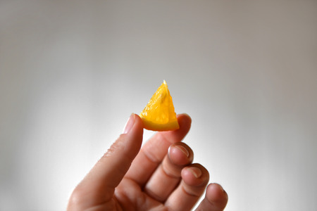 A small slice of orange in hands on a gray background. Orange in handの写真素材