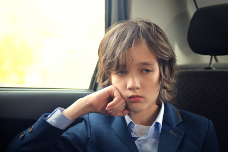 A boy is a teenager with a long hair in a classic suit in the car. Stylish child in the car.の写真素材