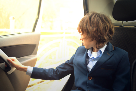 A boy is a teenager with a long hair in a classic suit in the car. Stylish child in the car.の写真素材
