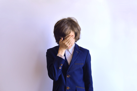 The schoolboy is in despair. The schoolboy is crying. Schoolboy in uniform with closed face on a white backgroundの写真素材