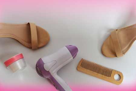 Set for woman. Female shoes, hair dryer, comb and cream on a pink and white background, top view, horizontal orientation.の写真素材
