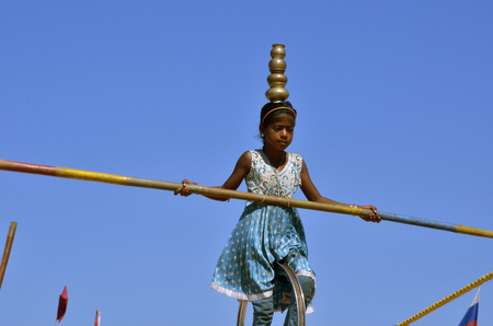 Panaji, Goa, India - 31/12/2011: A girl from India on a rope on a background of blue sky with a pole and a vase on her head in a blue dressのeditorial素材