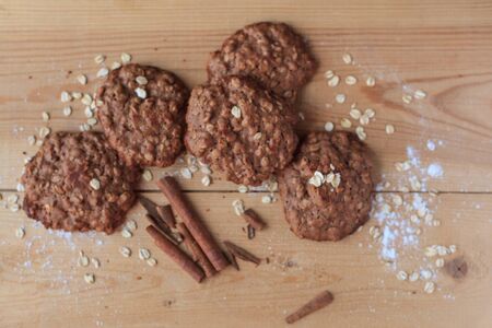Several traditional oatmeal cookies with cocoa, sprinkled with oatmeal flakes and flour, are on the wooden boards with cinnamon sticks.の写真素材