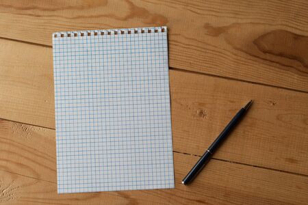 The ballpoint pen and the blank squared paper, which are from notebook, are on the wooden deskの写真素材