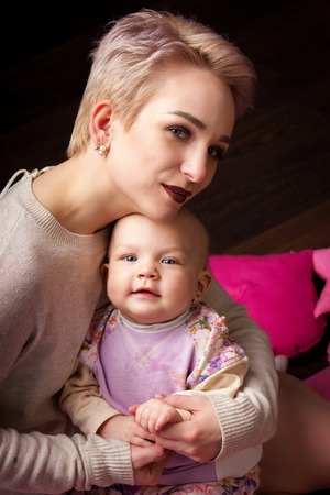 Attractive young mother playing with her daughter on the dark parquetの写真素材