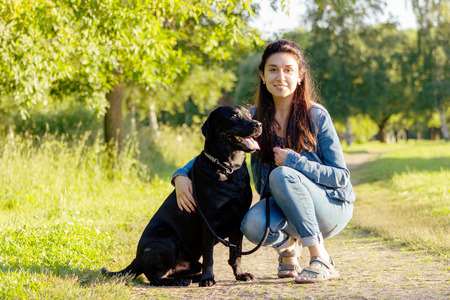 Beautiful young woman posing with her black labrador retriever on the pathway at summerの写真素材
