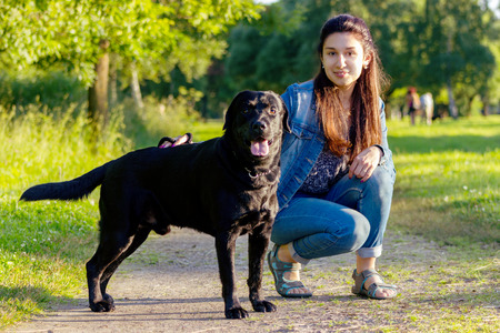 Beautiful young woman posing with her black labrador retriever on the pathway at summerの写真素材