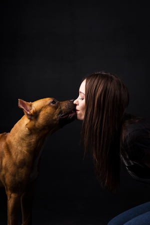 Girl kisses with red american staffordshire terrier indoor on black backgroundの写真素材
