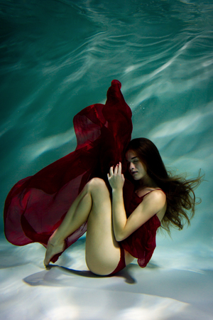 Dancing woman under the water in a pool in a red dress.の写真素材